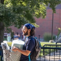 Man carries a laundry basket with stuff in it while student next to him